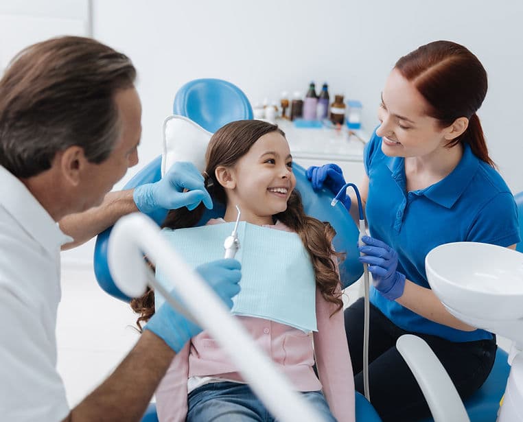 Dentistas atendendo uma paciente sorridente em um consultório moderno.
