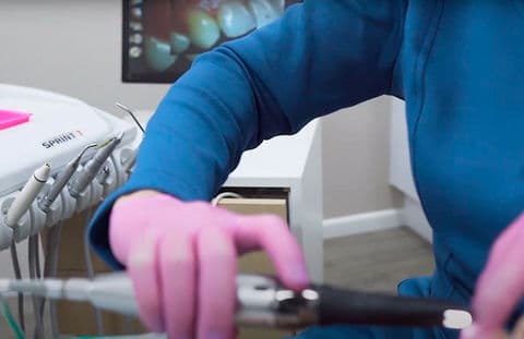 A imagem mostra um profissional manipulando um equipamento odontológico.